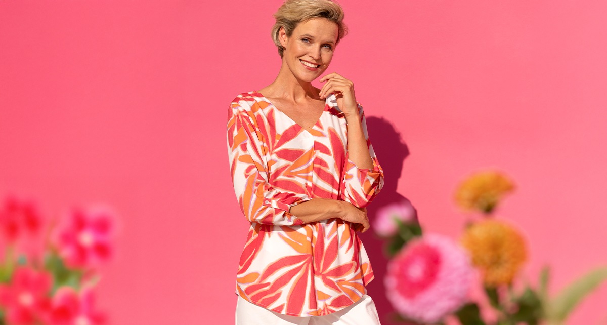 Dame in orange-weiß gemusterter Bluse vor einem rosa Hintergrund