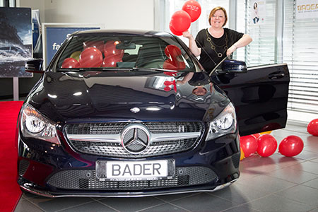 Gewinnspielübergabe vor einem mit roten Luftballons geschmückten Mercedes-Benz mit BADER-Kennzeichen; eine Frau steht an der geöffneten Fahrertür und hält Ballons.
